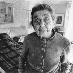 Svartvitt foto av en gammal, mycket rynkig kvinna som stillsamt betraktar fotografen