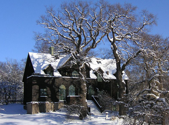 Samma stora mörka hus mot en klarblå himmel. Nu med taket och trädgården täckta av snö. De stora ekarna lövfria och också de täckta av ett tjockt lager snö