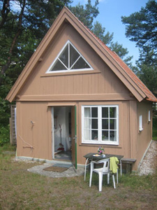 Gaveln på ett sandfärgat hus med brant sluttande tak, dörren står öppen, vita fönster, varav ett trekantigt ovan dörren