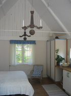 Ett vitmålat rum, öppet upp i nock, en säng, en korgstol och i fonden ett fönster