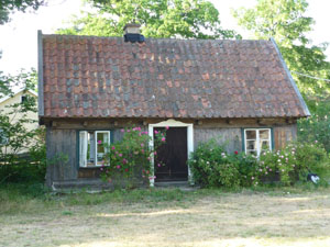 Ett litet omålat hus, ett brant tak täckt av gammalt tegel, rosor på var sida om den bruna dörren och på båda sidor ett fönster
