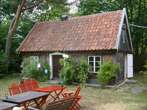 Ett litet omålat hus, ett brant tak täckt av gammalt tegel, rosor på var sida om den bruna dörren och på båda sidor ett fönster.